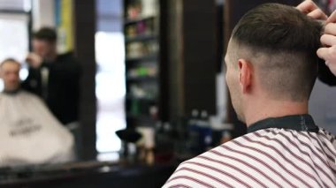 Genç bir erkek berber erkek bir müşterinin saçını düzeltir. Profesyonel saç bakım ürünleri. Bir berberin sinematik yakın çekimi erkek müşteriye soluk saç tıraşı yapıyor. Kısa kırpıcı saç stilinin yavaş çekim görüntüsü.