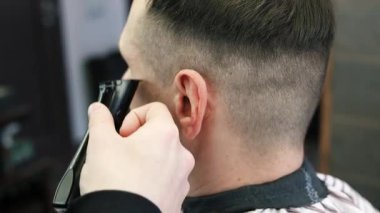 Genç bir erkek berber erkek bir müşterinin saçını düzeltir. Profesyonel saç bakım ürünleri. Bir berberin sinematik yakın çekimi erkek müşteriye soluk saç tıraşı yapıyor. Kısa kırpıcı saç stilinin yavaş çekim görüntüsü.