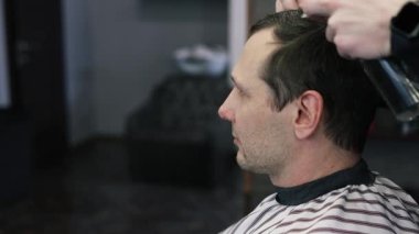 Genç bir erkek berber erkek bir müşterinin saçını düzeltir. Profesyonel saç bakım ürünleri. Bir berberin sinematik yakın çekimi erkek müşteriye soluk saç tıraşı yapıyor. Kısa kırpıcı saç stilinin yavaş çekim görüntüsü.