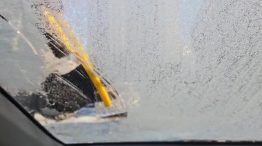 Arabanın içinden, otomobil temizleme fırçası kullanan bir adama yakın plan, arabanın ön camındaki karı temizler. Kış arabası ön camları siliyor. Kışın iyi görünmesi için arabadan karı temizlemek..