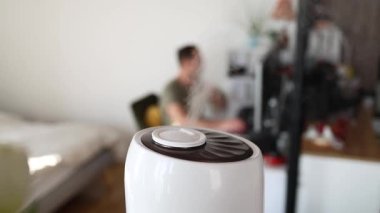 Oturma yerinde modern hava nemlendirici cihazı, internet üzerinde bilgisayar kullanan genç adam, ana ofisteki gerekli yağ dağıtıcıdan gelen aromaterapi buhar kokusunun tadını çıkarıyor..