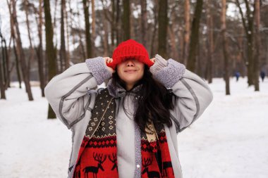 Mutlu gülümseyen genç Asyalı kadın kar, kış parkında sıcak hava, kışın ormanda örgü şapkalı gülen kadın..