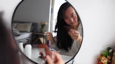 Güzel Asyalı orta yaşlı kadın dışarı çıkmaya hazırlanıyor, sabah makyajını yapıyor ve banyoda aynanın karşısına fırçayla yüz pudrası sürüyor..