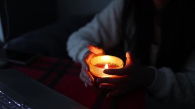 Elektrik kesintisinde elinde mum tutan stresli bir adam. Güç durumu yok. Donmuş genç adam evdeki kanepede dizüstü bilgisayar kullanıyor. Ukrayna 'daki savaştan dolayı karartma.