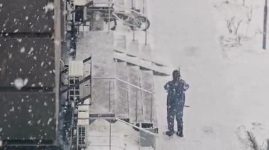 Karlı şehir manzarası, yüksek binalar ve kar manzaralı bir pencere. Şehir ve binalar karla kaplıyken manzara sakin ve huzurlu.