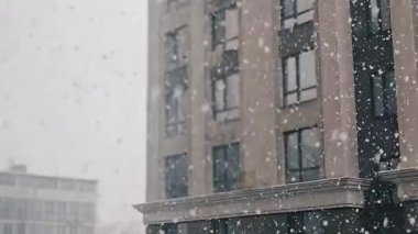 Karlı şehir manzarası, yüksek binalar ve kar manzaralı bir pencere. Şehir ve binalar karla kaplıyken manzara sakin ve huzurlu.