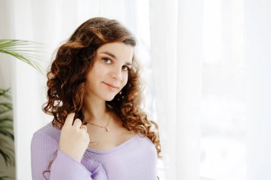 Esmer kadın uzun kıvırcık saçlarını parlak ve davetkar bir odada şımartırken gülümsüyor. Kendine baktığı sırada güzellik ve kendine güven saçıyor..