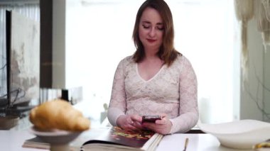 Kadın, akıllı telefon ve kahve fincanı mutfakta, mesajlaşmalı, iletişim kurmalı ya da sosyal medyada yazmalı. Mobil uygulama ile okuma, blog yazma ve içme, paylaşımı veya tebligatı evde gülümseme ile paylaşma