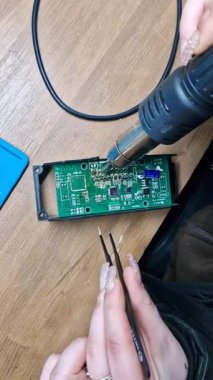 Kurulum atölyesindeki aletlerle çevrili basılı devre kartını ustalıkla lehimleyen kadın bir teknisyenin yakın çekimi. Dikey video.