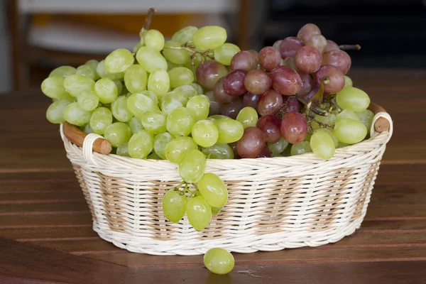 Gröna och röda druvor i en flätad korg. — Stockfoto