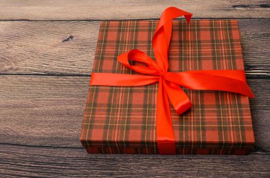 Ahşap masa üzerinde kırmızı kurdele ile küçük hediye kutusu