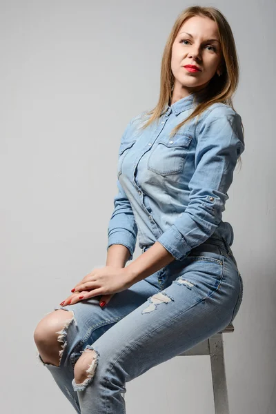 Glada blonda kvinnan ler, sitter i jeans. — Stockfoto