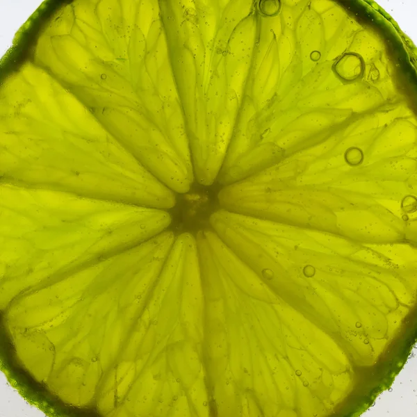 Piece of fresh juicy lime making bubbles in water — Stock Photo, Image