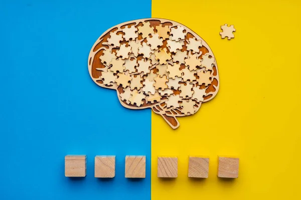 Mock up of a human brain with scattered puzzle pieces on a yellow and blue background. Six cubes in which you can write the word autism in your font.