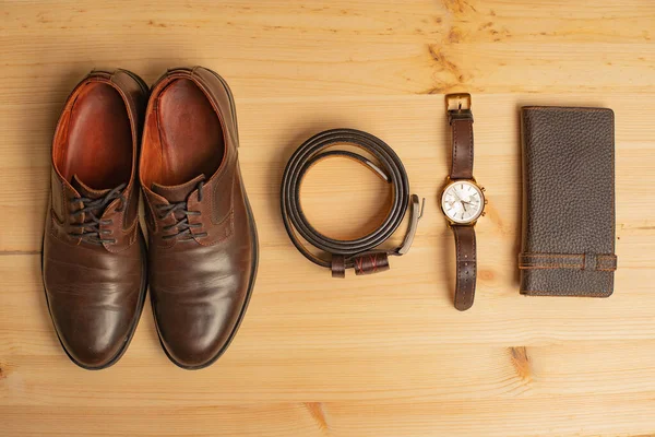 Men's accessories with brown leather wallet, belt, shoes and watch on wooden background