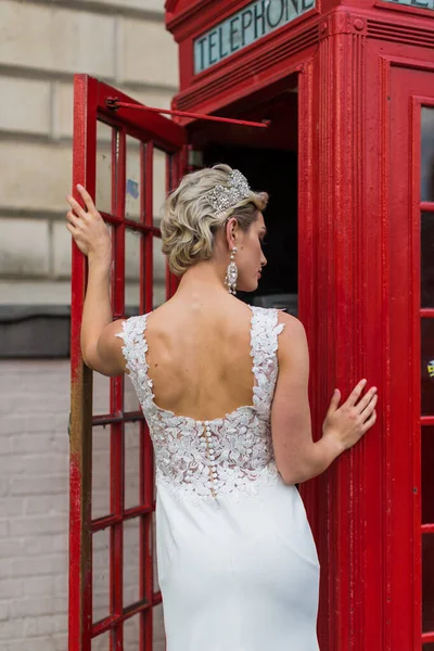 the bride in a white dress enters the red phone cabin
