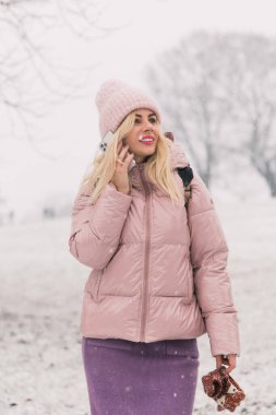 Pudra ceketli kadın telefonda konuşuyor, kışın arka planda.