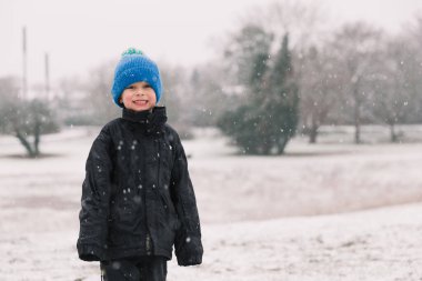 Siyah ceketli çocuk kışın gülümsüyor.
