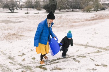 Anne ve oğul kızak çekerek tepeye çıkıyorlar.