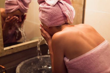 Banyoda yüzünü suyla yıkayan genç kadının yakın görüntüsü.