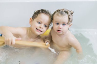 Komik küçük kız ve tatlı kardeşi duş aldıktan sonra köpükle birlikte suda oynayarak eğleniyorlar..