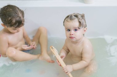 Komik küçük kız ve tatlı kardeşi duş aldıktan sonra köpükle birlikte suda oynayarak eğleniyorlar..