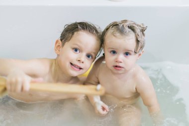 Komik küçük kız ve tatlı kardeşi duş aldıktan sonra köpükle birlikte suda oynayarak eğleniyorlar..