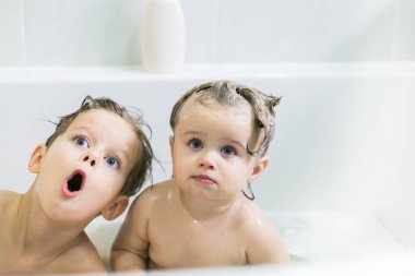 Komik küçük kız ve tatlı kardeşi duş aldıktan sonra köpükle birlikte suda oynayarak eğleniyorlar..