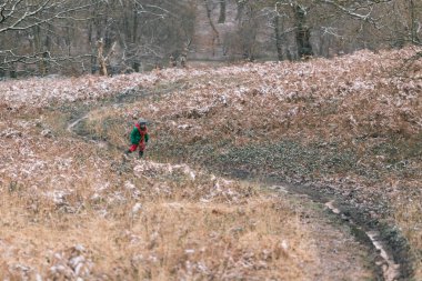 Sıcak giyimli çocuk kışın ormanda koşuyor.