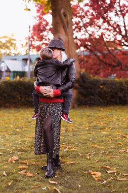 Anne, oğlunu sonbahar parkında kollarında tutuyor.