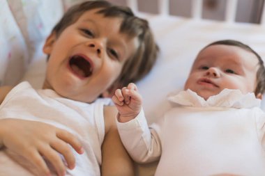 Mutlu çocuklar. Oğlan ve bebek yatakta uzanıyorlar. Gülümsüyor. 3-4 yıl. Neşeli bir aile. Oyuncaklar.