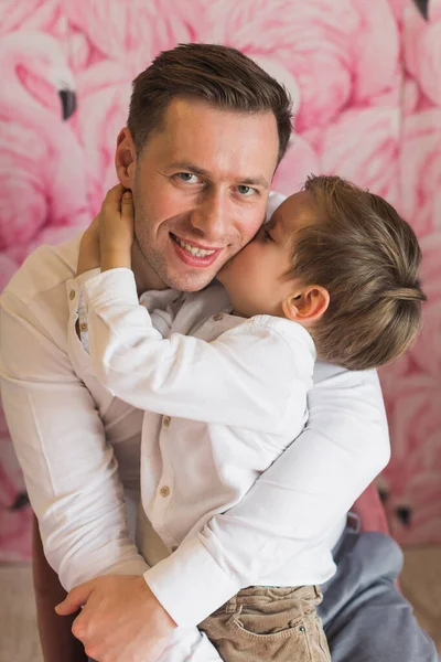 Family. Father and son. The son hugs and kisses the father. A happy family. Smile. Background. Pink.