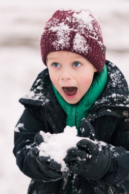 Mutlu çocuk kışın dışarıda oynarken eğleniyor. Kış tatilleri ve tatiller. Karı ellerinde tutuyor..