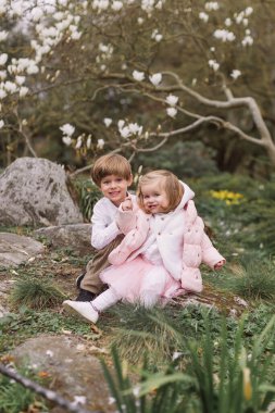 Parkta eğlenen mutlu çocuklar. Oturuyorum. Küçük kız ve oğlan dışarıda birlikte oynuyorlar. Manolya çiçekleri.
