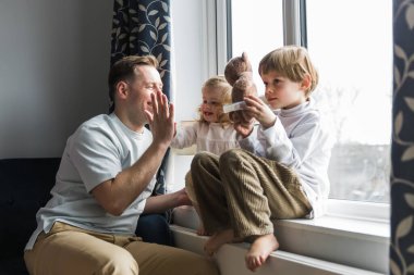 Çocuklar pencere eşiğine oturur. Mutlu baba çocuklarla oynuyor. Beş veriyor. Bir kız ve bir erkek oynuyorlar..
