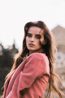 Klasik pembe ceketli, güzel, esmer bir kızın portresi. Düşünceli bir bakış. Kameraya bak. Arkaplan mimarisi.