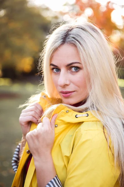 黄色のジャケットに魅力的な若いブロンドの女性の肖像画 カメラを見てください 秋の公園の背景 — ストック写真