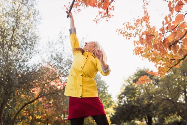 Young blonde woman in a yellow jacket having fun in the park. Standing. Autumn park background.