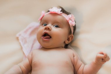 Çiçek çelenginde yeni doğmuş bir bebek. Yatakta yatarken. Dil çıkarıyorum. Çırılçıplak. Hafif bir arkaplanda.