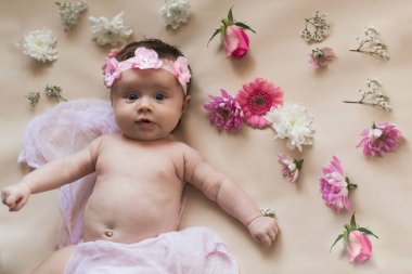 Çiçek çelenginde yeni doğmuş bir bebek. Çiçeklerle yatakta yatmak. Çırılçıplak. Hafif bir arkaplanda.