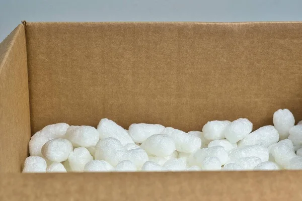 White packing peanuts styrofoam popcorn packaging material inside a cardboard box, angle view with copy space.