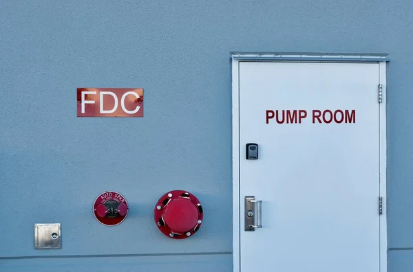 Fire pump room door with signs and wall fixtures on an industrial warehouse exterior.