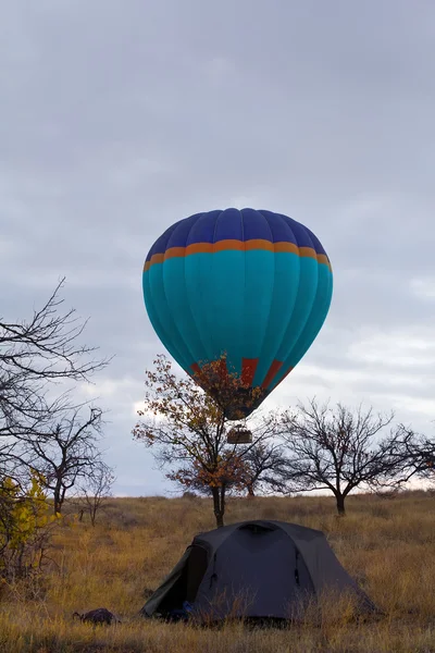 Varm luft ballon flyver over turist telt på Kappadokien Tyrkiet - Stock-foto