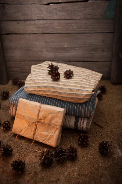 Stapel van kleren met denneappels en gift op houten achtergrond — Stockfoto