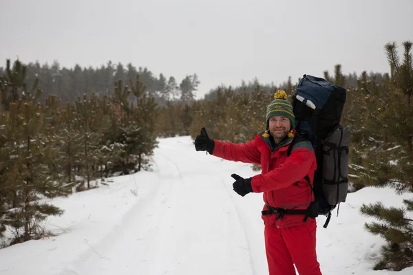 Hombre con una mochila autostop en el bosque de invierno —  Fotos de Stock
