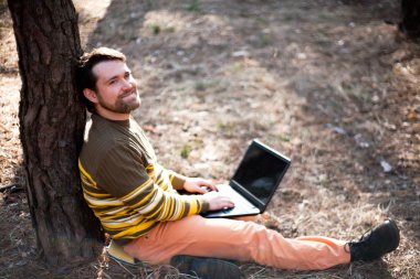 Mutlu adam açık havada bir dizüstü bilgisayar kullanarak oturuyor