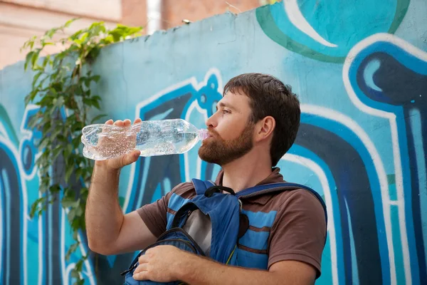 Jonge man drinkwater uit plastic flessen op achtergrond met graffiti — Stockfoto