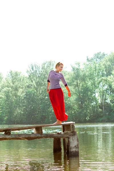 Pretty young woman in red dress posing on the pier — Stock Fotó