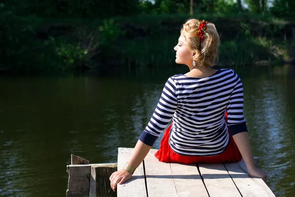 Pretty young woman in red dress sitting on pier — Stock Fotó