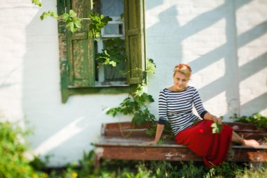 Beautiful girl sitting on bench near rural house